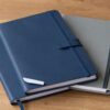 Agendas y libretas corporativas de tapa dura apiladas sobre un escritorio de madera