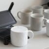 Prensa de tazas cerrada sobre una taza blanca con papel de transferencia en un taller