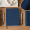 Regalos corporativos sobre un escritorio: termo de acero, libreta, boligrafo, tote bag y gorra