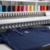 Maquina bordadora industrial cosiendo un emblema sobre un polo azul marino