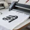 Plancha termica aplicando vinil de corte sobre una camiseta blanca en un taller